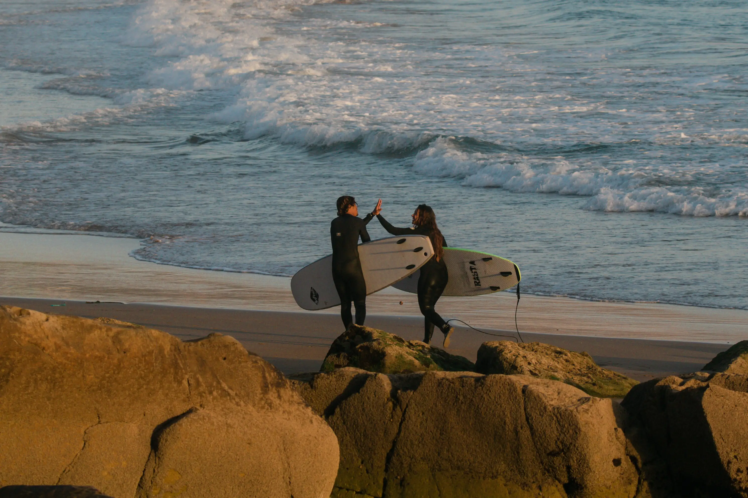 Green Waves Morocco surfers high-fiving after a surf session on the beach in Tamraght Morocco with Atlantic waves in the background